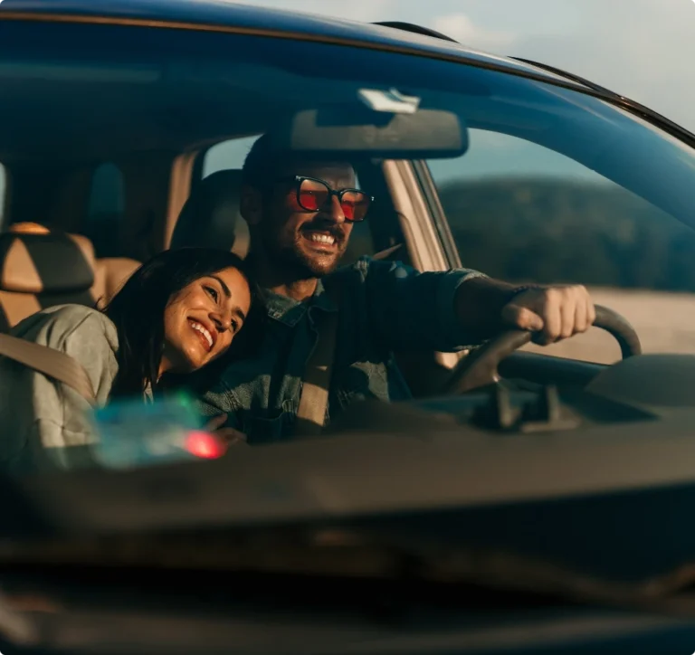 Leende par kör bil i solnedgång efter service hos Autoexperten Huskvarna.